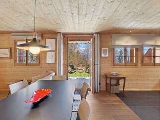 Experience cozy living in this charming wooden cabin, featuring a spacious dining area with a modern pendant light and a direct view to the outdoors.
