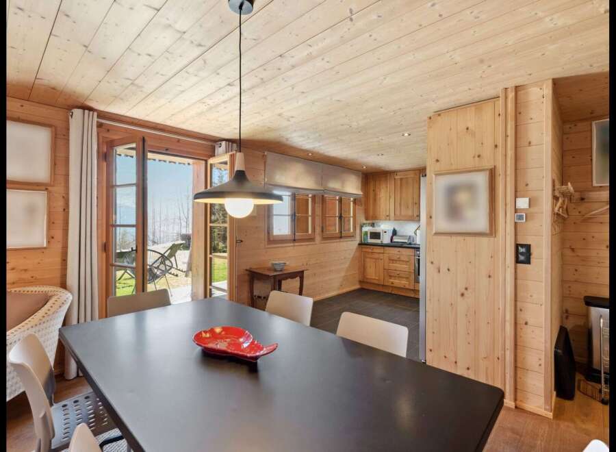 Experience cozy living in this charming wooden cabin, featuring a spacious dining area with a dark wood table and comfortable seating.