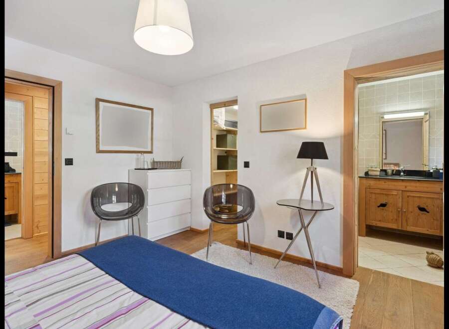 This charming bedroom features a comfortable bed with a blue throw, complemented by two modern transparent chairs and a white dresser.