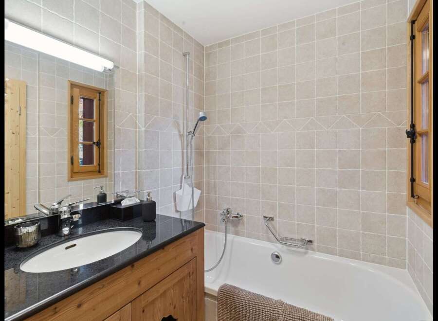This charming bathroom features a sleek vanity with a granite countertop and an undermount sink, complemented by a large mirror and overhead lighting.
