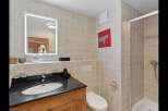 This modern bathroom features a sleek vanity with a granite countertop and an undermount sink, complemented by a large, illuminated mirror.