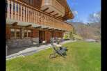 Experience alpine living in this charming wooden chalet featuring a stone facade and a spacious balcony overlooking a lush green lawn.