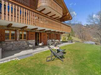 Experience alpine living in this charming wooden chalet featuring a stone facade and a spacious balcony overlooking a lush green lawn.