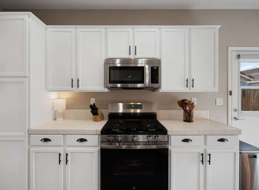 This kitchen features sleek white cabinetry with modern black hardware, complemented by a stainless steel microwave and gas range.