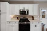 This kitchen features sleek white cabinetry with modern black hardware, complemented by a stainless steel microwave and gas range.