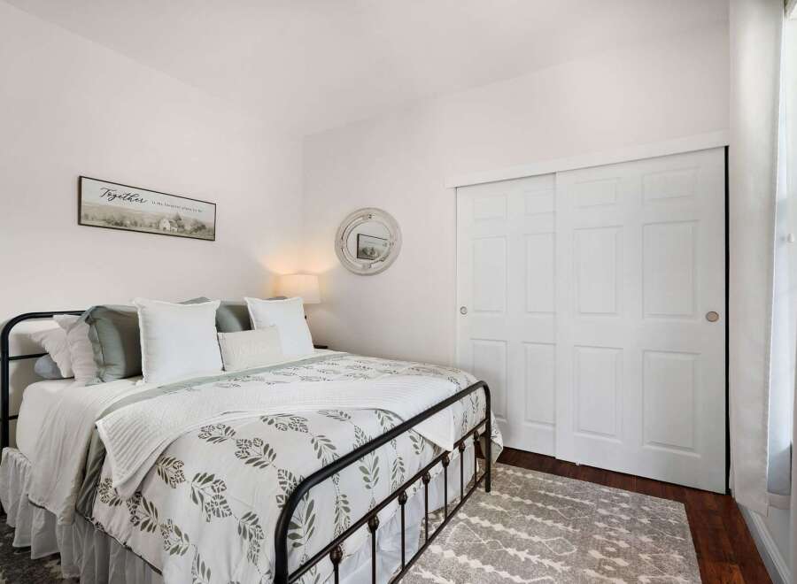 This charming bedroom features a cozy queen-size bed with a decorative metal frame, adorned with plush pillows and a botanical-print comforter.
