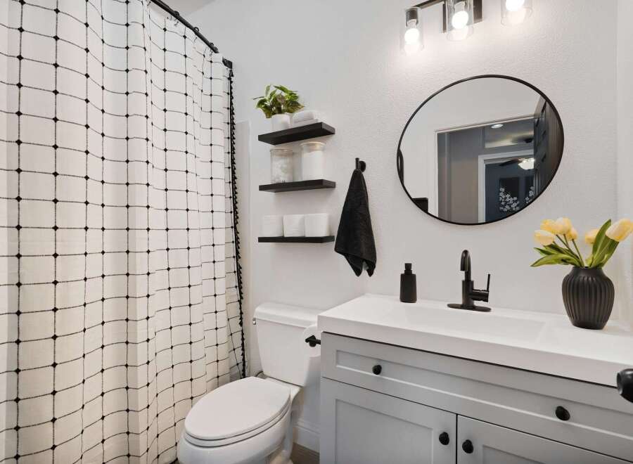 This modern bathroom features a stylish gray vanity with black hardware, complemented by a white countertop and a sleek black faucet.