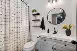 This modern bathroom features a stylish gray vanity with black hardware, complemented by a white countertop and a sleek black faucet.