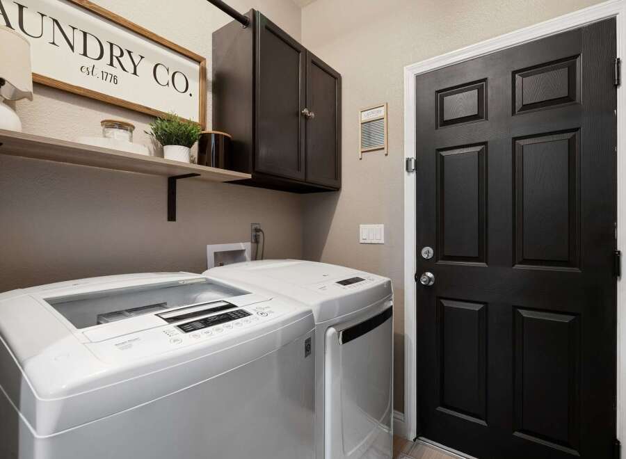 This laundry room features a white top-load washing machine and dryer, complemented by a dark wood cabinet for storage.