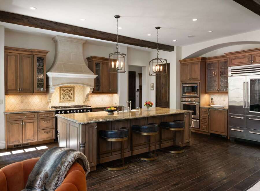 Experience luxury in this stunning gourmet kitchen, featuring custom wood cabinetry, a grand stone range hood, and a spacious granite island perfect for entertaining.