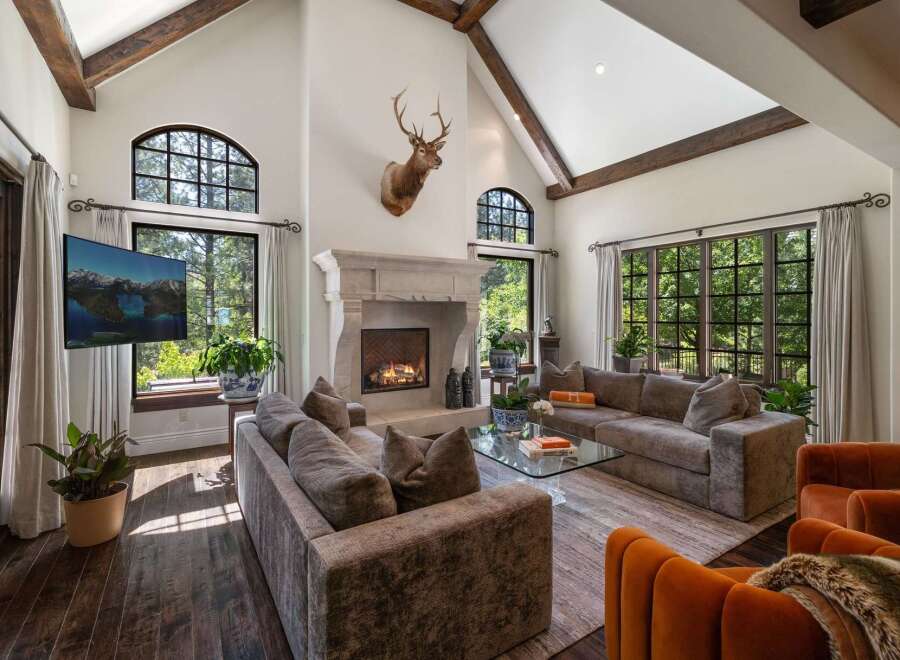 Experience luxurious mountain living in this stunning great room, featuring a grand stone fireplace and soaring vaulted ceilings with exposed wooden beams.