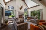 Experience luxurious mountain living in this stunning great room, featuring a grand stone fireplace and soaring vaulted ceilings with exposed wooden beams.