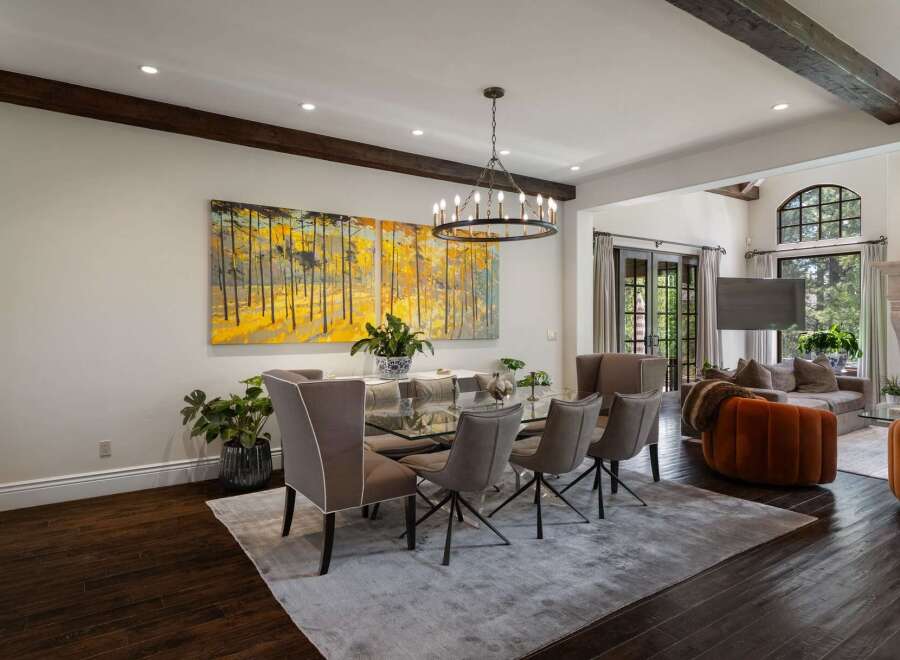 Experience elegant dining in this spacious room featuring a modern glass-top dining table with sleek chairs, illuminated by a striking circular chandelier.