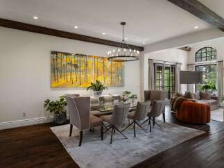 Experience elegant dining in this spacious room featuring a modern glass-top dining table with sleek chairs, illuminated by a striking circular chandelier.