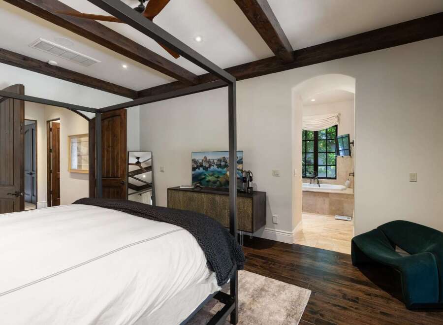 Experience luxurious living in this master suite featuring a grand four-poster bed and exposed wooden beams.
