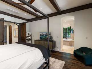 Experience luxurious living in this master suite featuring a grand four-poster bed and exposed wooden beams.