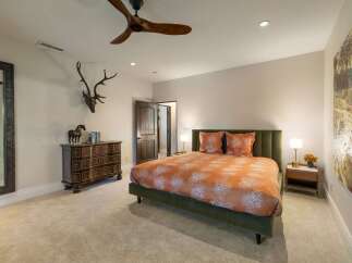 This master bedroom offers a luxurious retreat with a plush green upholstered bed adorned with vibrant orange patterned bedding.
