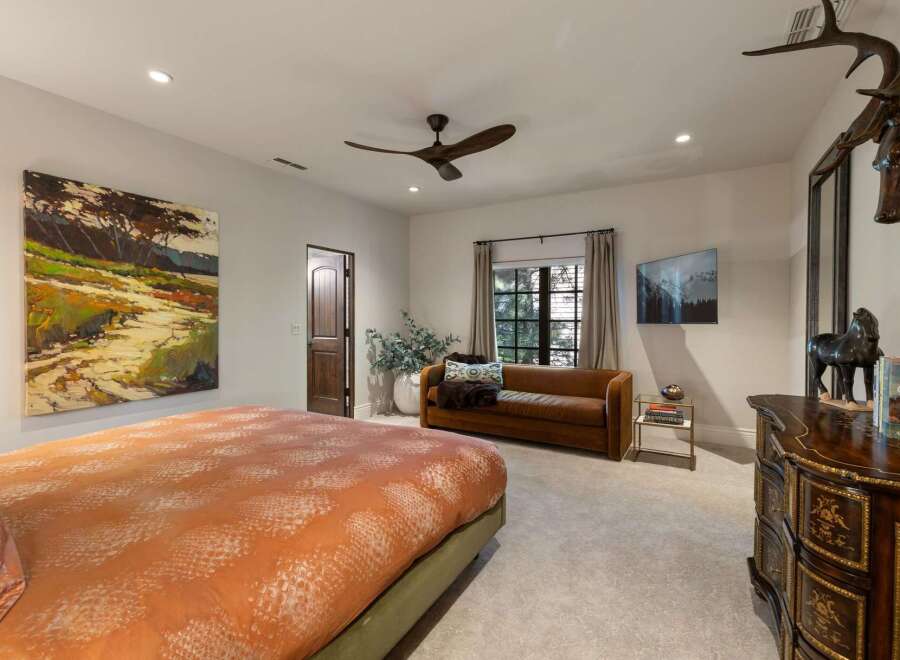 This luxurious bedroom features a large, abstract landscape painting above a king-sized bed with a vibrant orange and white patterned comforter.
