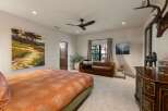 This luxurious bedroom features a large, abstract landscape painting above a king-sized bed with a vibrant orange and white patterned comforter.