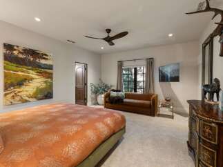This luxurious bedroom features a large, abstract landscape painting above a king-sized bed with a vibrant orange and white patterned comforter.