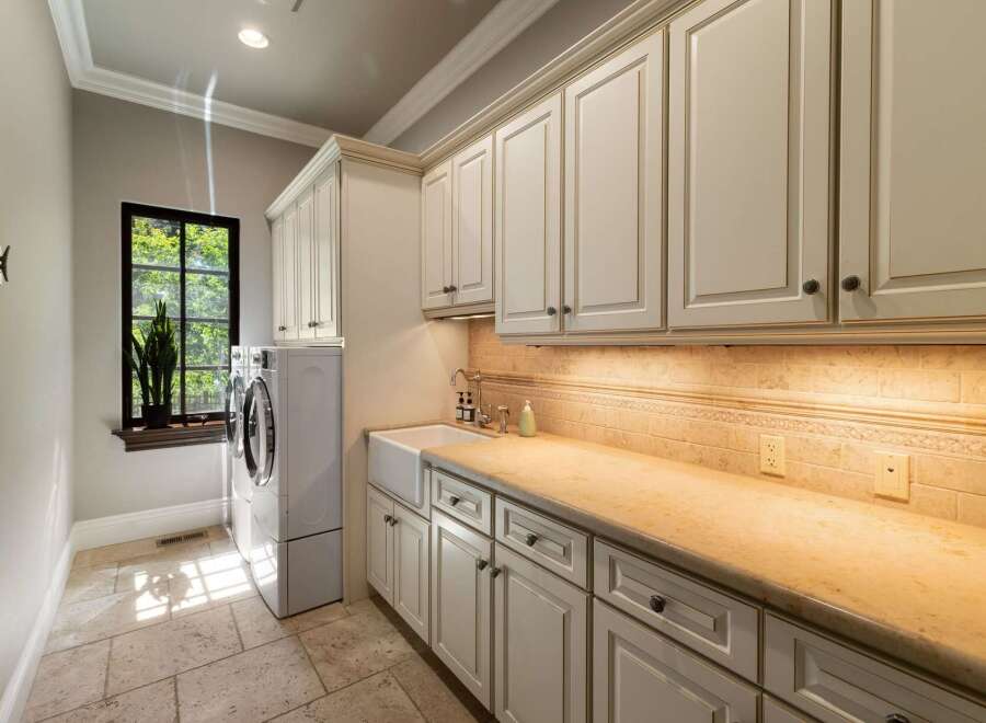 This laundry room boasts ample storage with custom cream-colored cabinetry, both above and below the countertop.