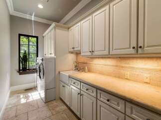 This laundry room boasts ample storage with custom cream-colored cabinetry, both above and below the countertop.