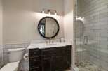 This charming bathroom features a dark wood vanity with a marble countertop, complemented by a round black framed mirror and a three-light vanity light fixture.