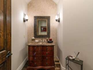 Discover this elegant powder room featuring a charming vanity with a marble countertop and ornate wooden drawers.