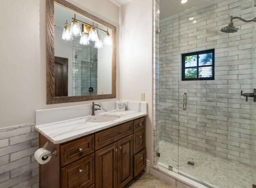 This modern bathroom features a spacious vanity with a marble countertop and a dark wood cabinet, complemented by a large rustic mirror with a multi-light fixture.