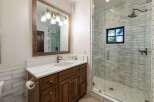 This modern bathroom features a spacious vanity with a marble countertop and a dark wood cabinet, complemented by a large rustic mirror with a multi-light fixture.