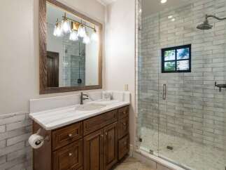 This modern bathroom features a spacious vanity with a marble countertop and a dark wood cabinet, complemented by a large rustic mirror with a multi-light fixture.