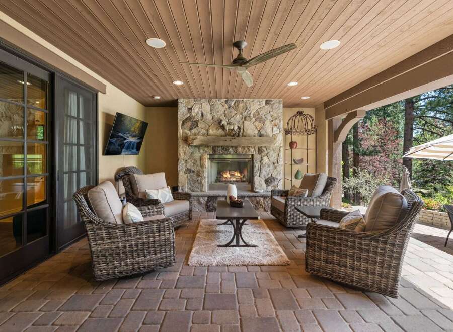 Experience ultimate outdoor living with this covered patio, featuring a cozy stone fireplace and comfortable wicker seating.