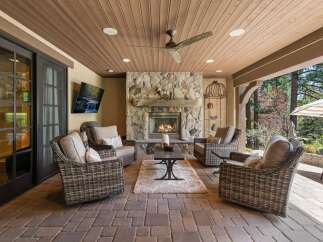 Experience ultimate outdoor living with this covered patio, featuring a cozy stone fireplace and comfortable wicker seating.