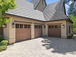 This stunning property features a spacious three-car garage with elegant wooden doors and decorative windows, perfect for housing multiple vehicles.