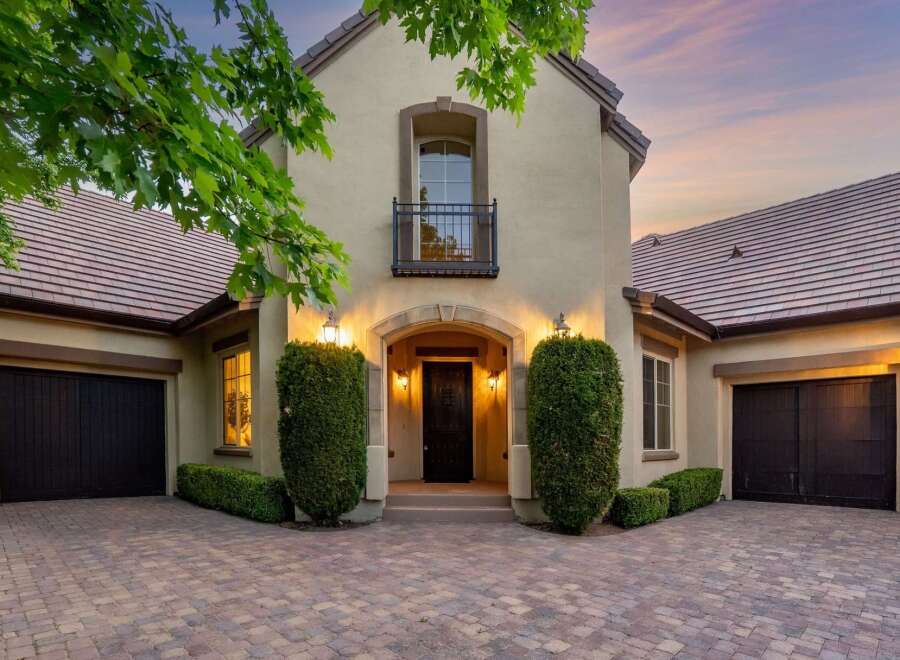 This stunning home features a grand arched entryway leading to a beautifully lit front door, flanked by manicured hedges.