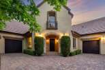 This stunning home features a grand arched entryway leading to a beautifully lit front door, flanked by manicured hedges.