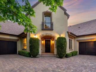 This stunning home features a grand arched entryway leading to a beautifully lit front door, flanked by manicured hedges.
