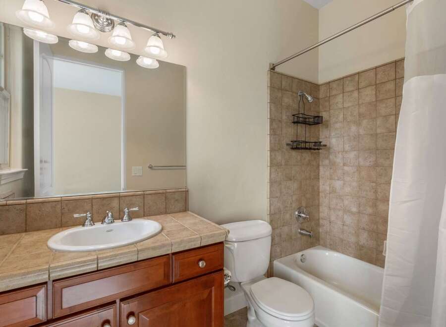 This bathroom features a spacious vanity with a white oval sink and a tiled countertop, complemented by a large mirror with a vanity light fixture above.