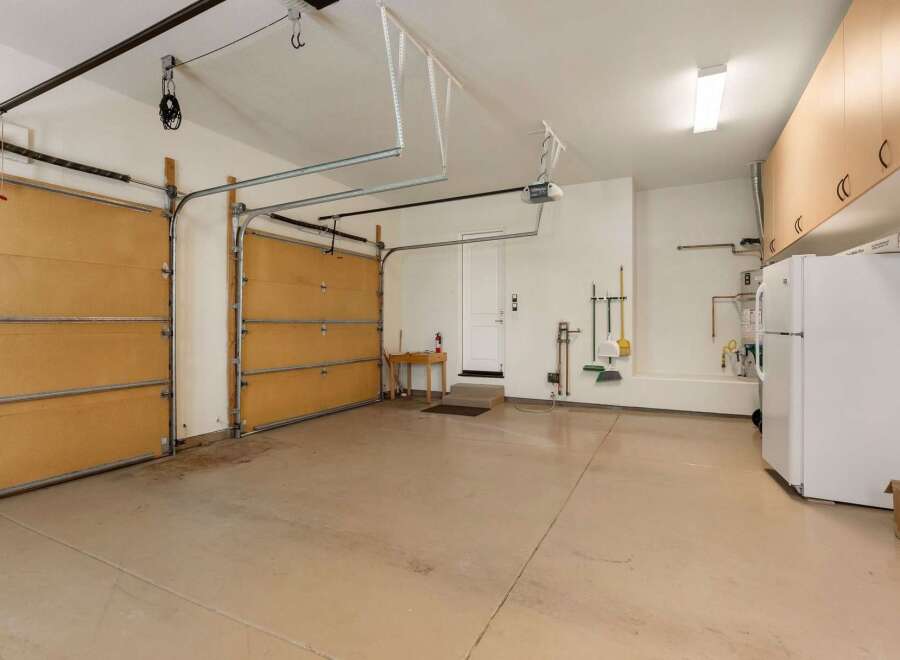 This spacious garage offers ample storage with overhead cabinets and a convenient workbench area.