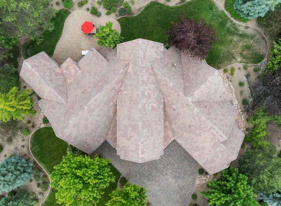 Discover this stunning aerial view of a uniquely designed home with a complex roofline, surrounded by lush greenery and mature trees.