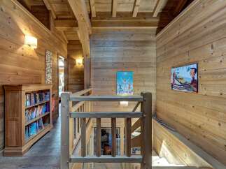 Experience rustic charm in this wooden chalet hallway, featuring a cozy bookshelf filled with books and two elegant wall sconces.