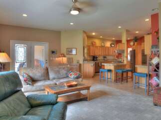 This open-concept living and kitchen area boasts a spacious living room with comfortable seating and a coffee table, seamlessly flowing into a well-equipped kitchen with ample cabinet space and a breakfast bar.