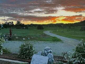 Experience breathtaking sunsets from this serene rural property, featuring rolling green hills and a winding gravel road leading to distant homes.