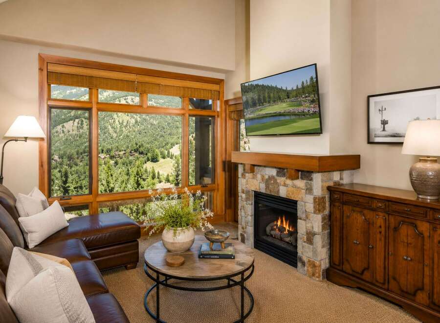 Experience luxury mountain living with this stunning living room featuring a cozy stone fireplace and a large window offering breathtaking views of the surrounding landscape.