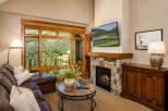 Experience luxury mountain living with this stunning living room featuring a cozy stone fireplace and a large window offering breathtaking views of the surrounding landscape.