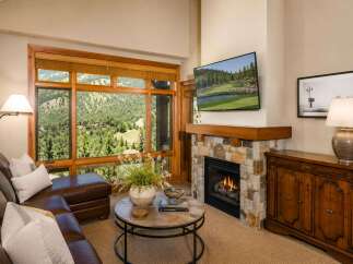 Experience luxury mountain living with this stunning living room featuring a cozy stone fireplace and a large window offering breathtaking views of the surrounding landscape.