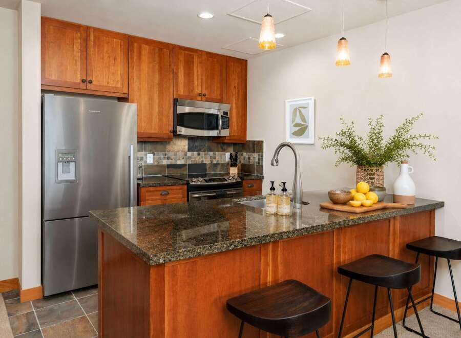 This modern kitchen features warm cherry wood cabinetry and a sleek granite countertop island, perfect for casual dining.