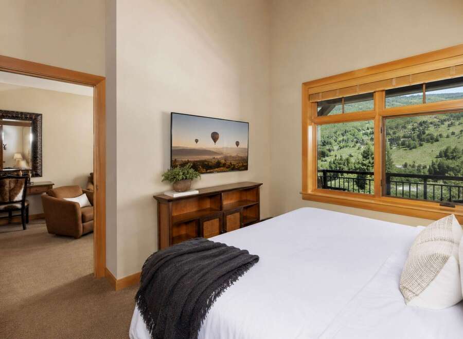 Experience breathtaking mountain views from this serene bedroom, featuring a large window overlooking lush greenery and a private balcony.