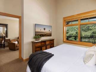 Experience breathtaking mountain views from this serene bedroom, featuring a large window overlooking lush greenery and a private balcony.