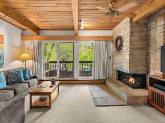 Experience cozy living in this inviting living room, featuring a stunning floor-to-ceiling stone fireplace and a warm, wood-paneled ceiling with exposed beams.